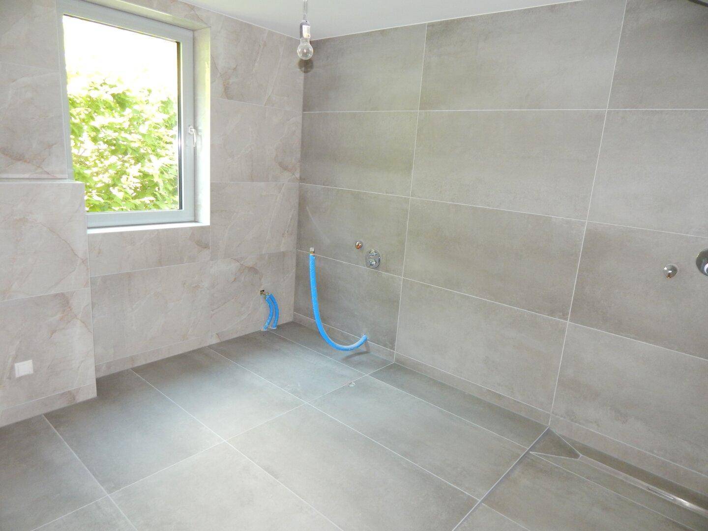 Geräumiges Badezimmer in Grau mit großen Fliesen und Vorbereitung für eine begehbare Dusche.