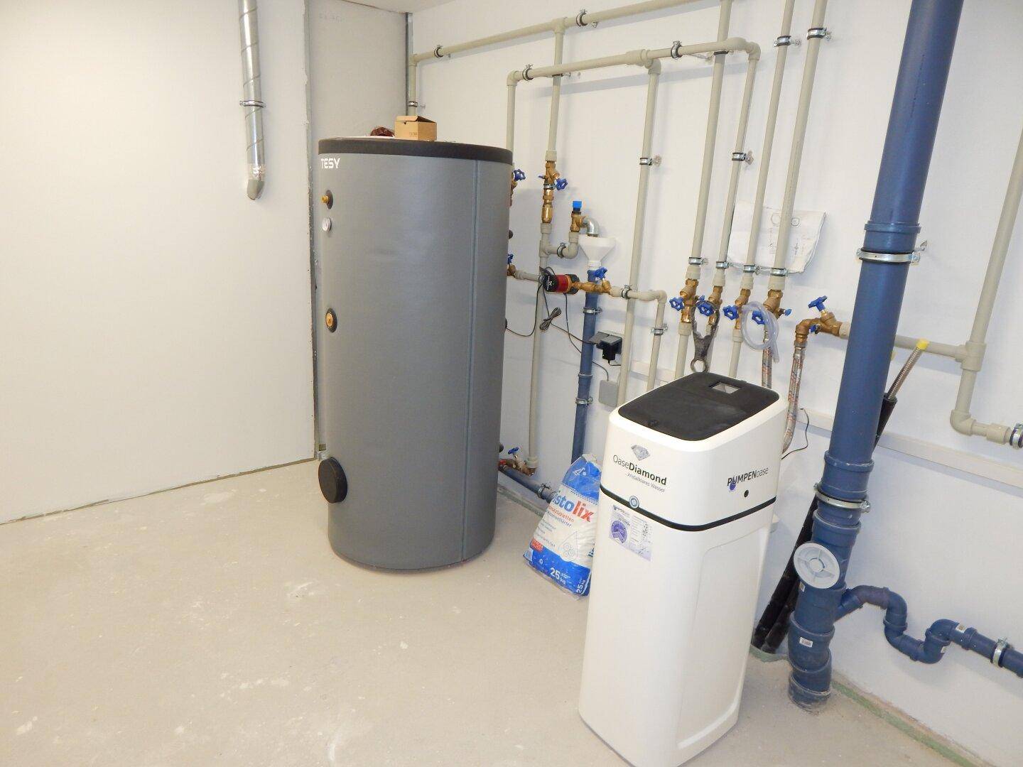 Technikraum mit Warmwasserspeicher, Wasserenthärtungsanlage und sichtbaren Rohrleitungen.