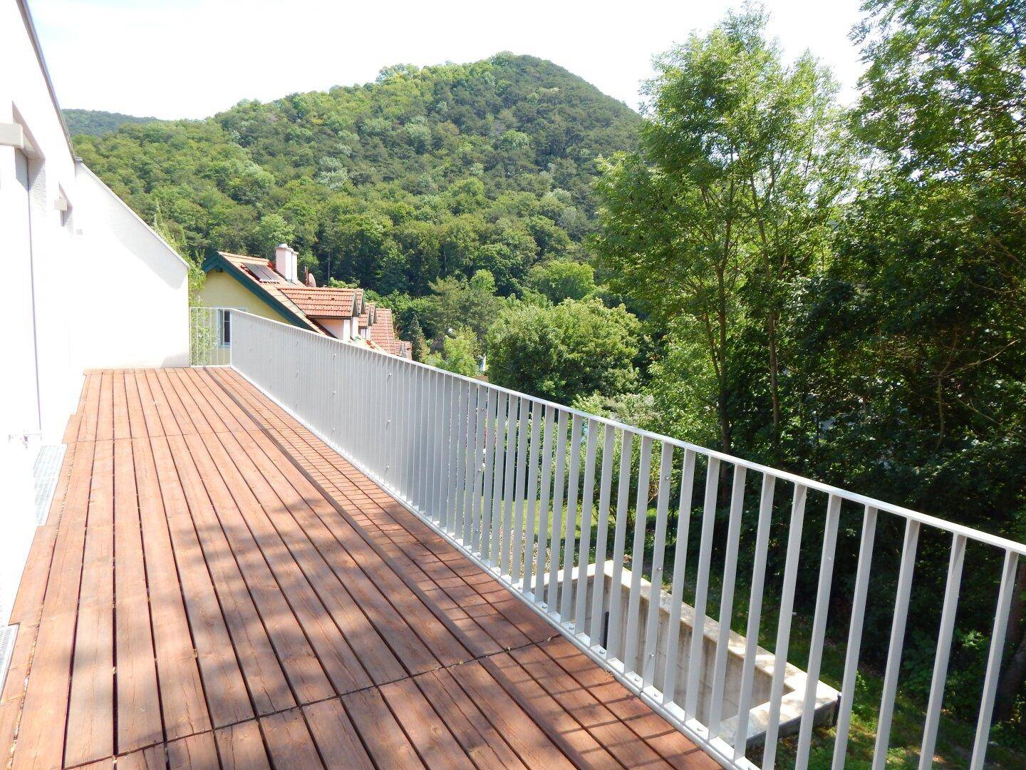 Geräumiger Holzbalkon mit Metallgeländer und weitem Blick auf bewaldete Hügel.