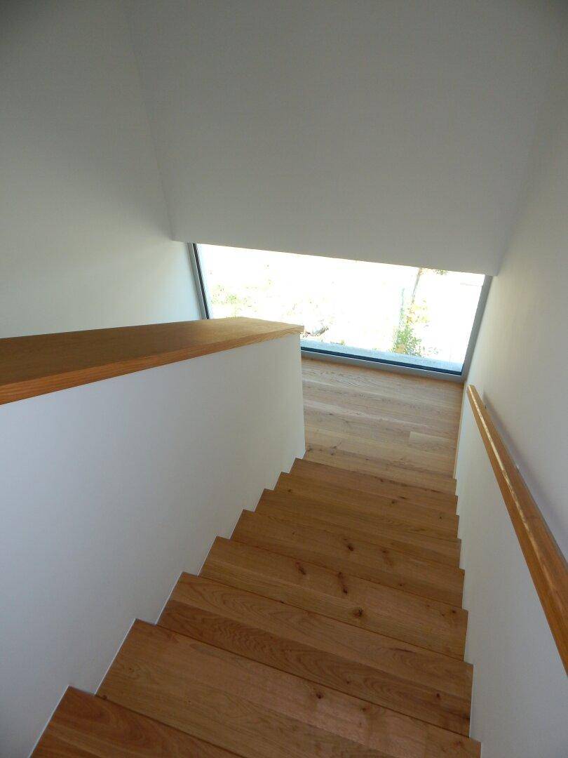 Moderne Holztreppe mit minimalistischem Design und großem Fenster für natürliche Belichtung.