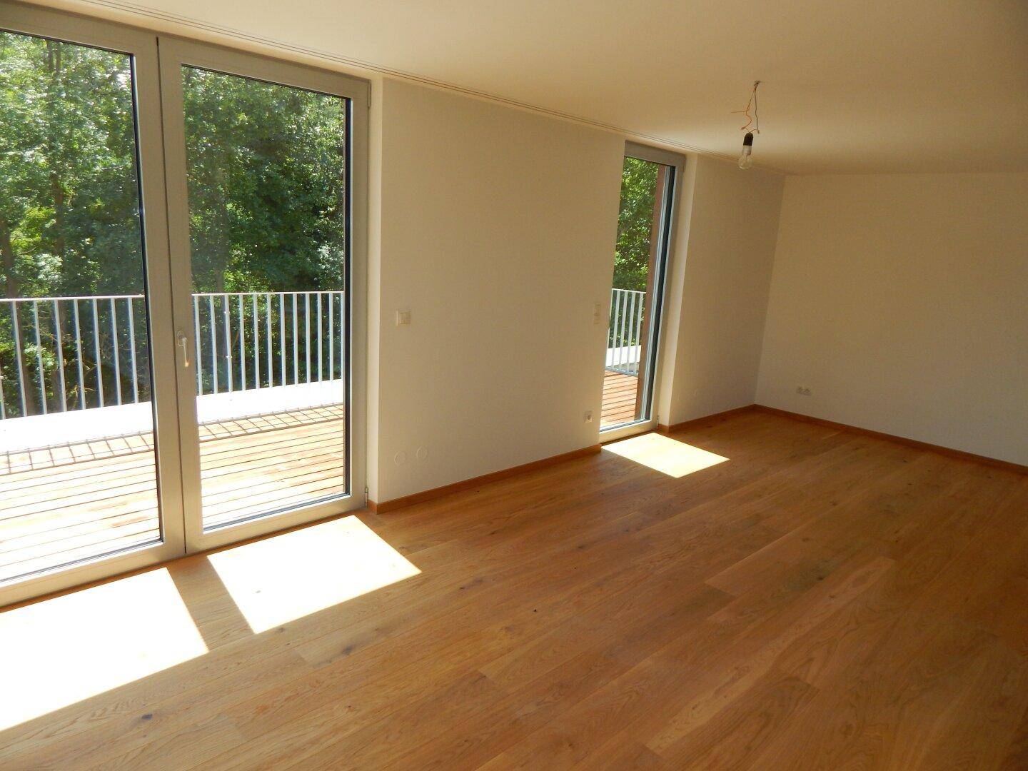 Helles Zimmer mit Holzparkett und Zugang zu einer Terrasse, durchflutet von Sonnenlicht.