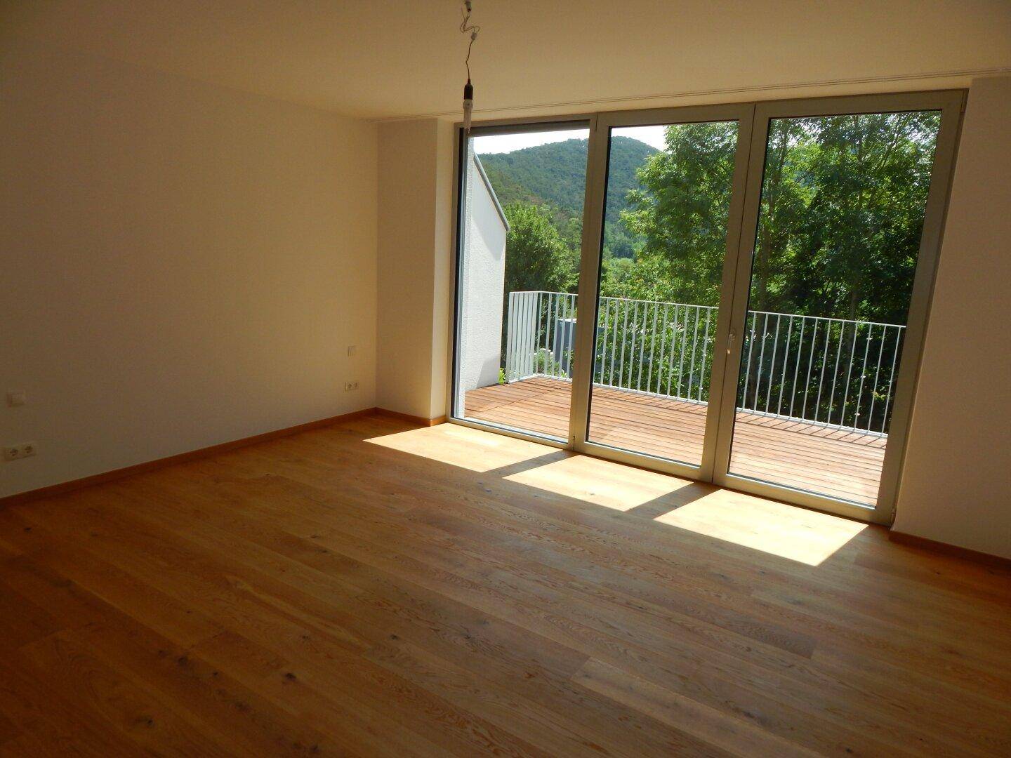 Geräumiges Zimmer mit Holzboden, großen Fenstern und Blick auf die grüne Hügellandschaft.
