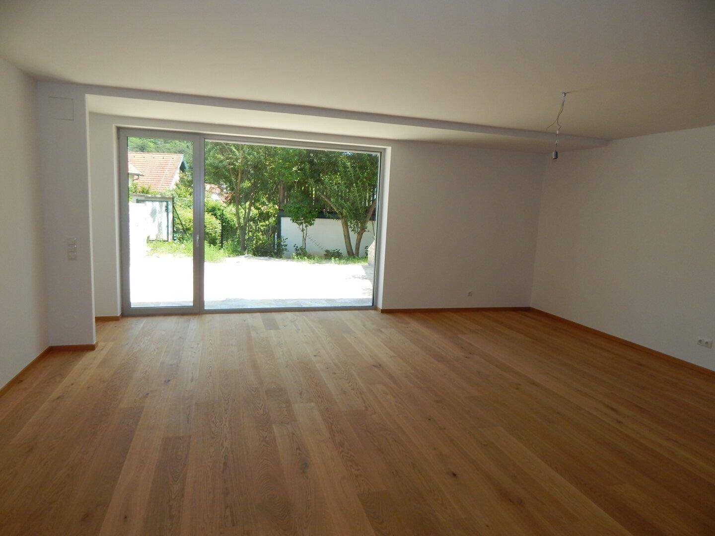 Heller Wohnraum mit Holzboden und großer Fensterfront, die den Blick ins Grüne öffnet.
