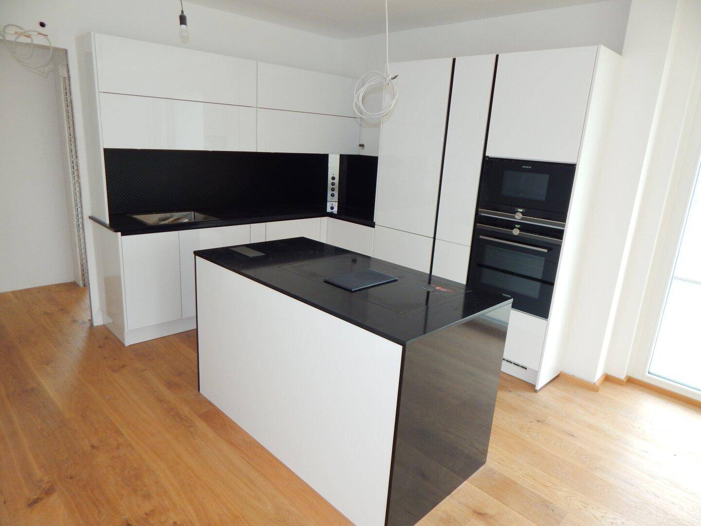 Moderne Küche mit weißen Hochglanzfronten, schwarzer Arbeitsplatte und Kochinsel.