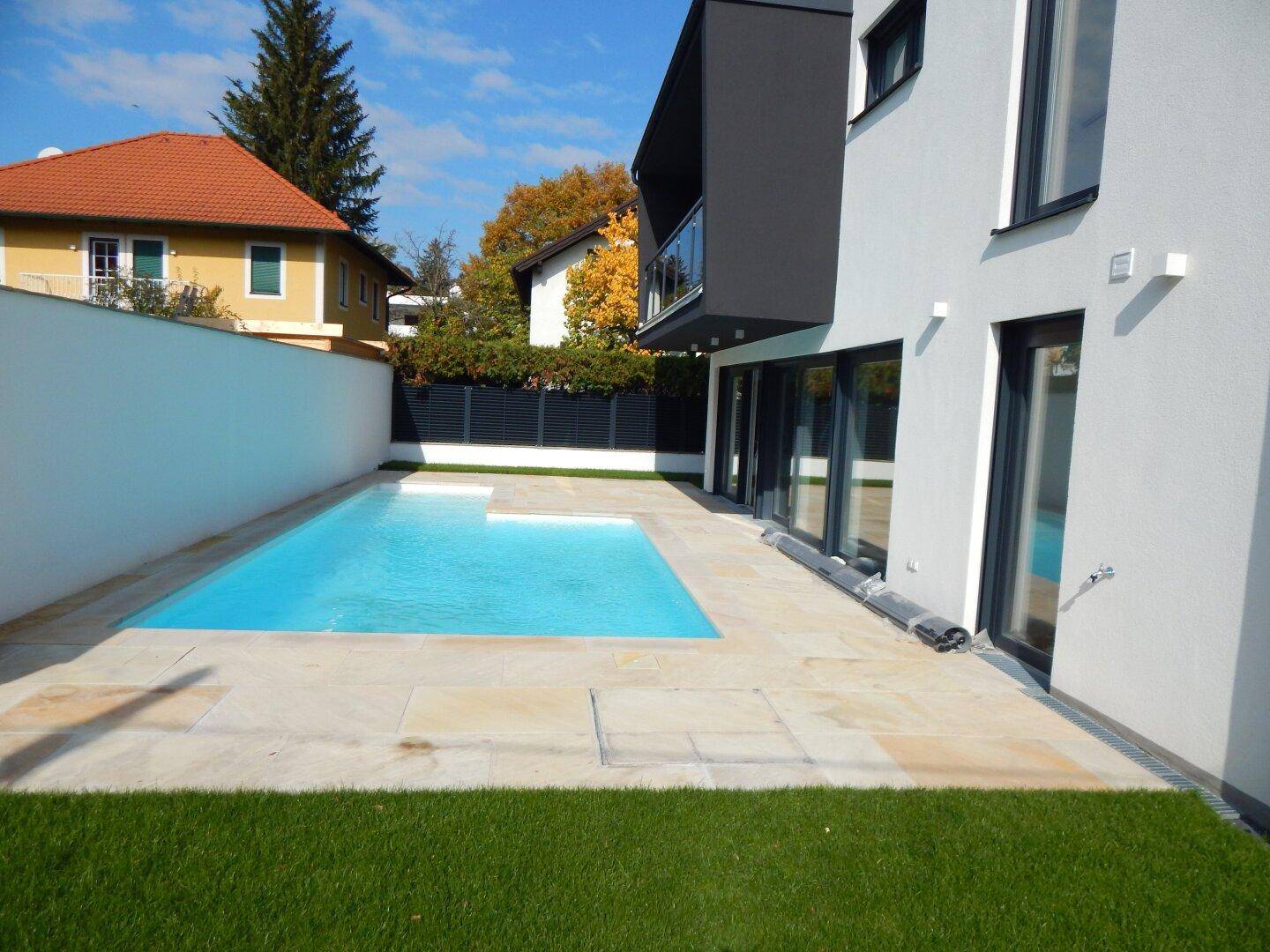 Der großzügige Poolbereich mit heller Steinterrasse und Rasenfläche lädt zum Entspannen ein.