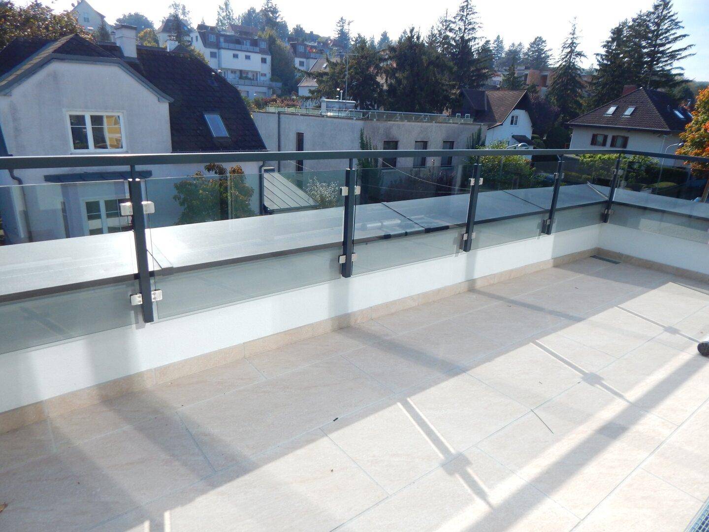 Großer Balkon mit moderner Glasbrüstung und hellem Fliesenboden, ideal für Entspannung.