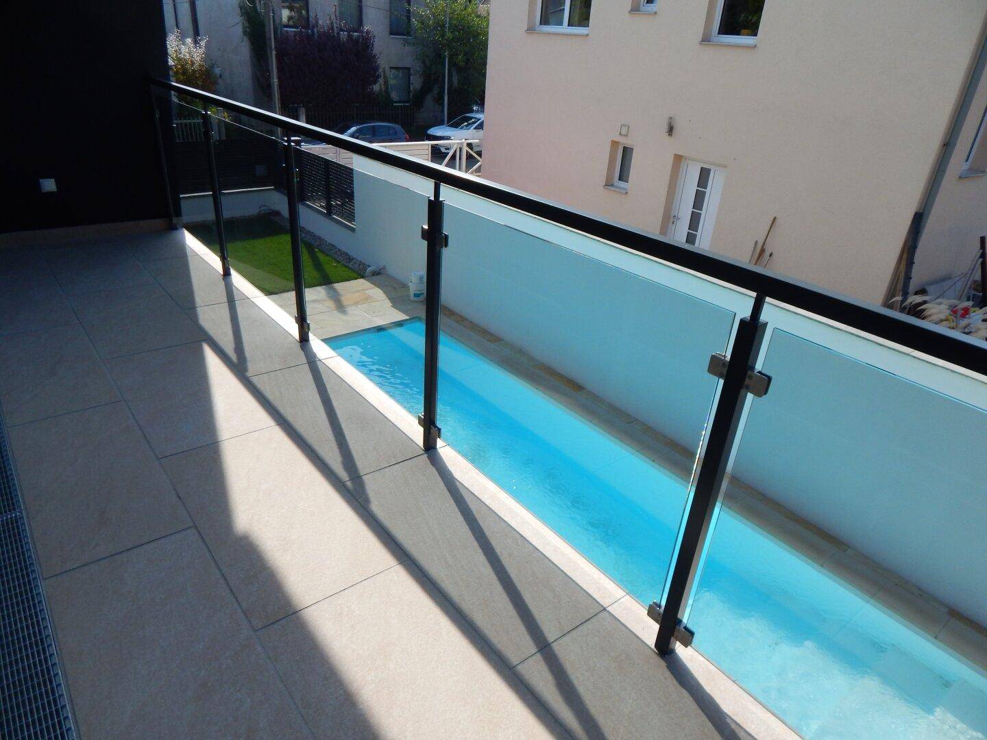 Moderner Balkon mit Glasgeländer und Blick auf den darunterliegenden Poolbereich des Hauses.