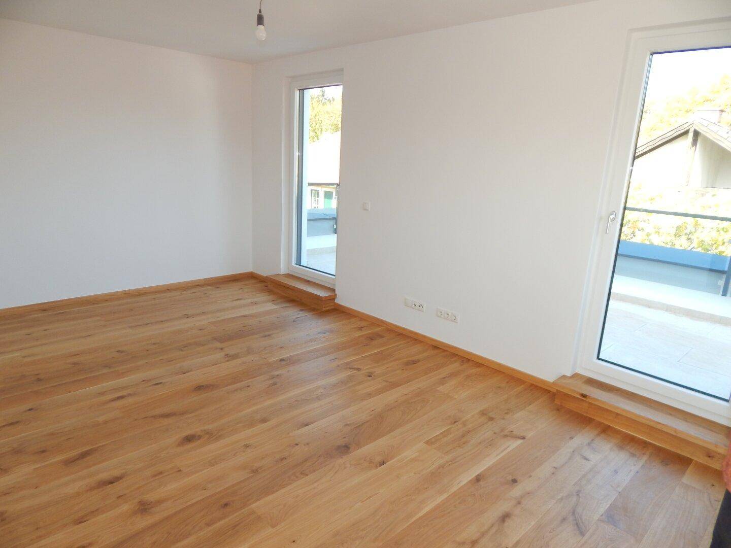 Helles Schlafzimmer mit hochwertigem Holzparkett und direktem Zugang zu einem Balkon.