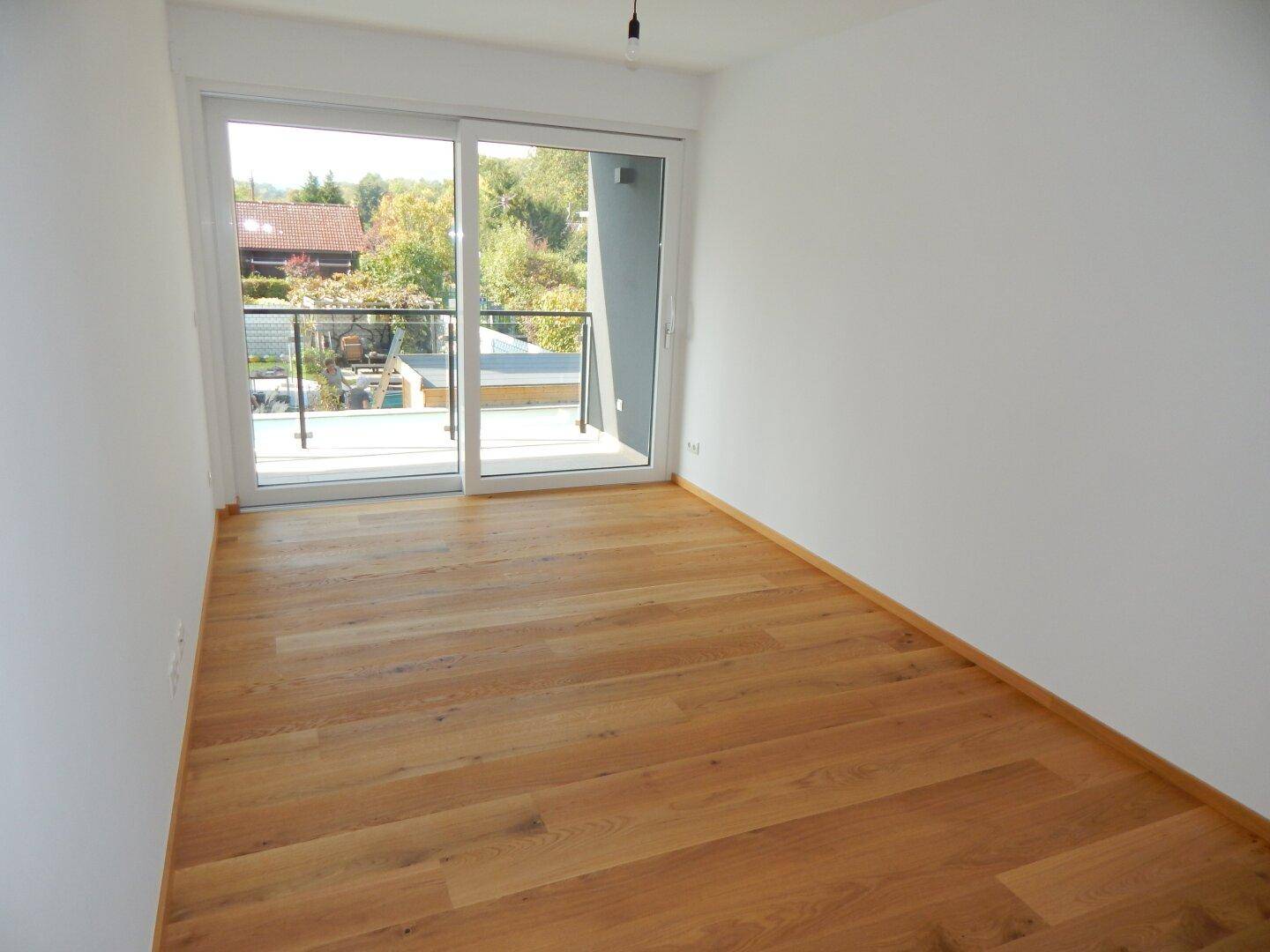 Geräumiges Schlafzimmer mit hellem Holzparkett und großen Schiebetüren zum Balkon.