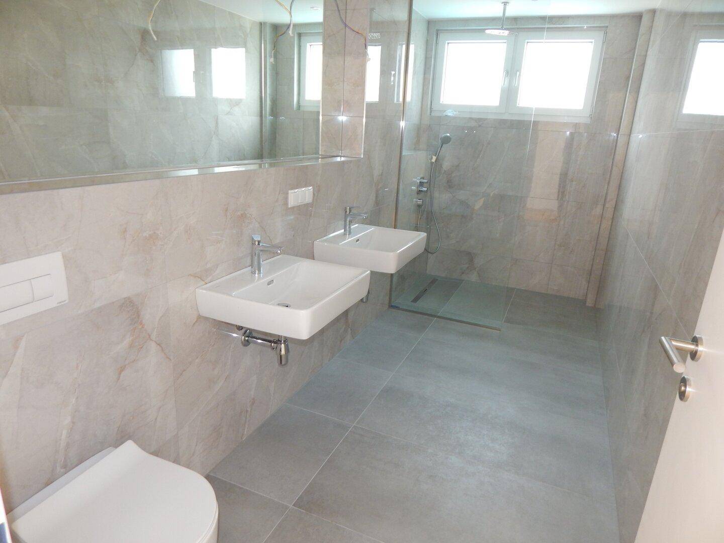 Modernes Badezimmer mit Doppelwaschbecken, wandhängendem WC und großer begehbarer Dusche.