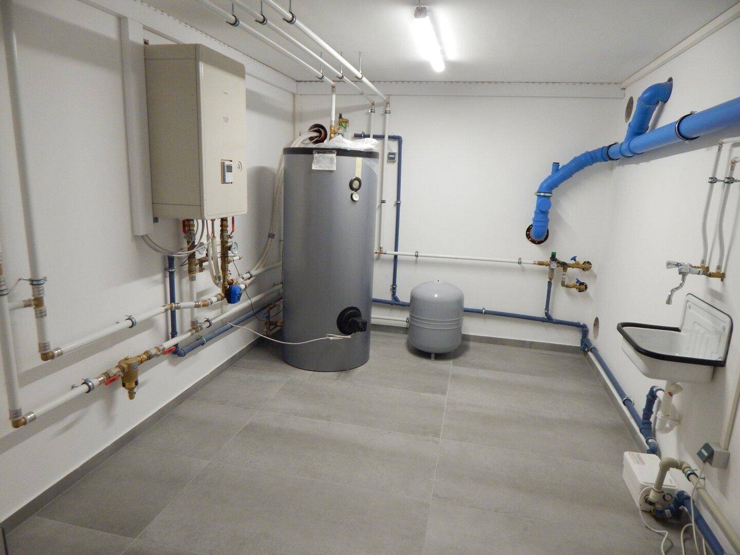 Technikraum mit Warmwasserspeicher und umfangreicher Rohrinstallation, sauber und funktional.