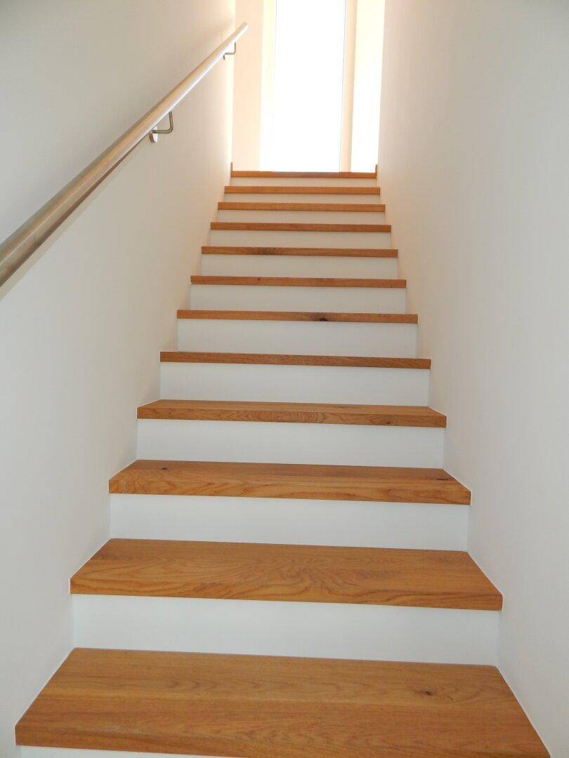 Elegante Holztreppe mit weiß gestrichenen Setzstufen und einem schlichten Handlauf.