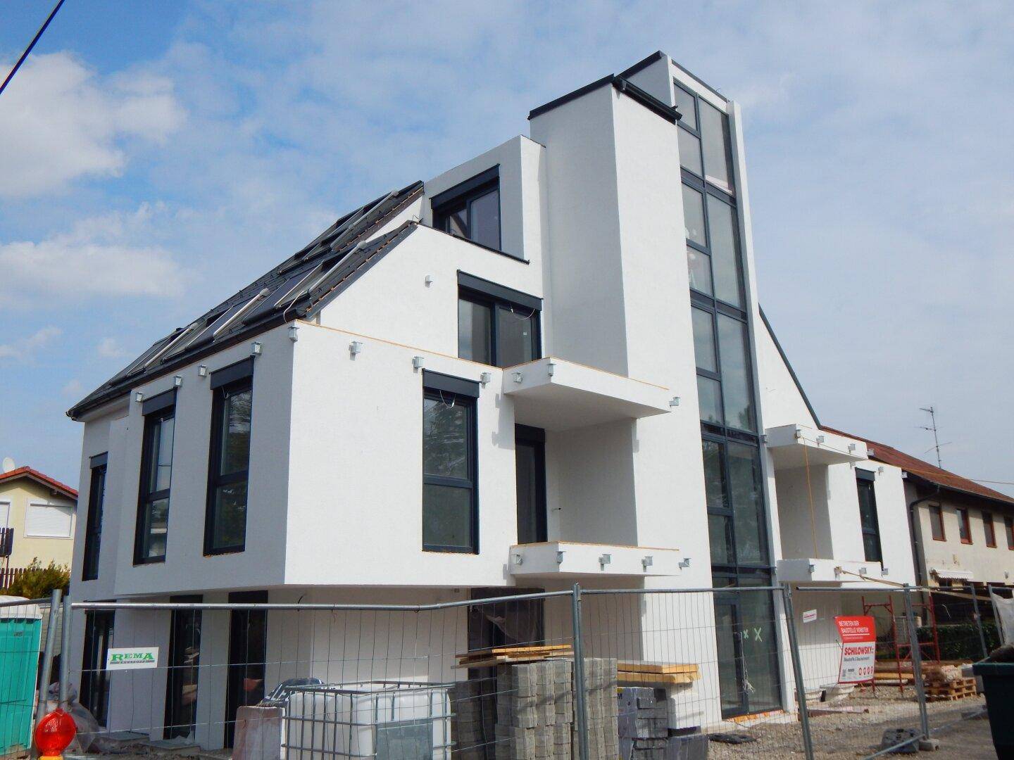 Neubau eines modernen Wohngebäudes mit weißer Fassade und großen Fenstern während der Bauphase.