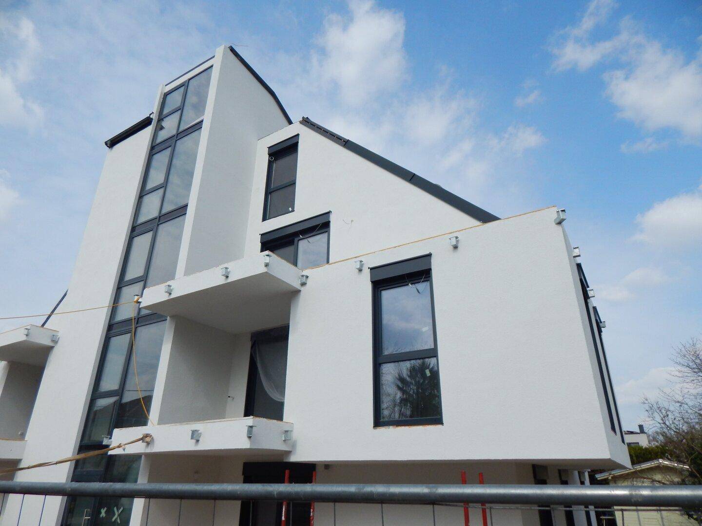 Moderne Architektur eines im Bau befindlichen Gebäudes mit weißer Fassade und großen Glasflächen.