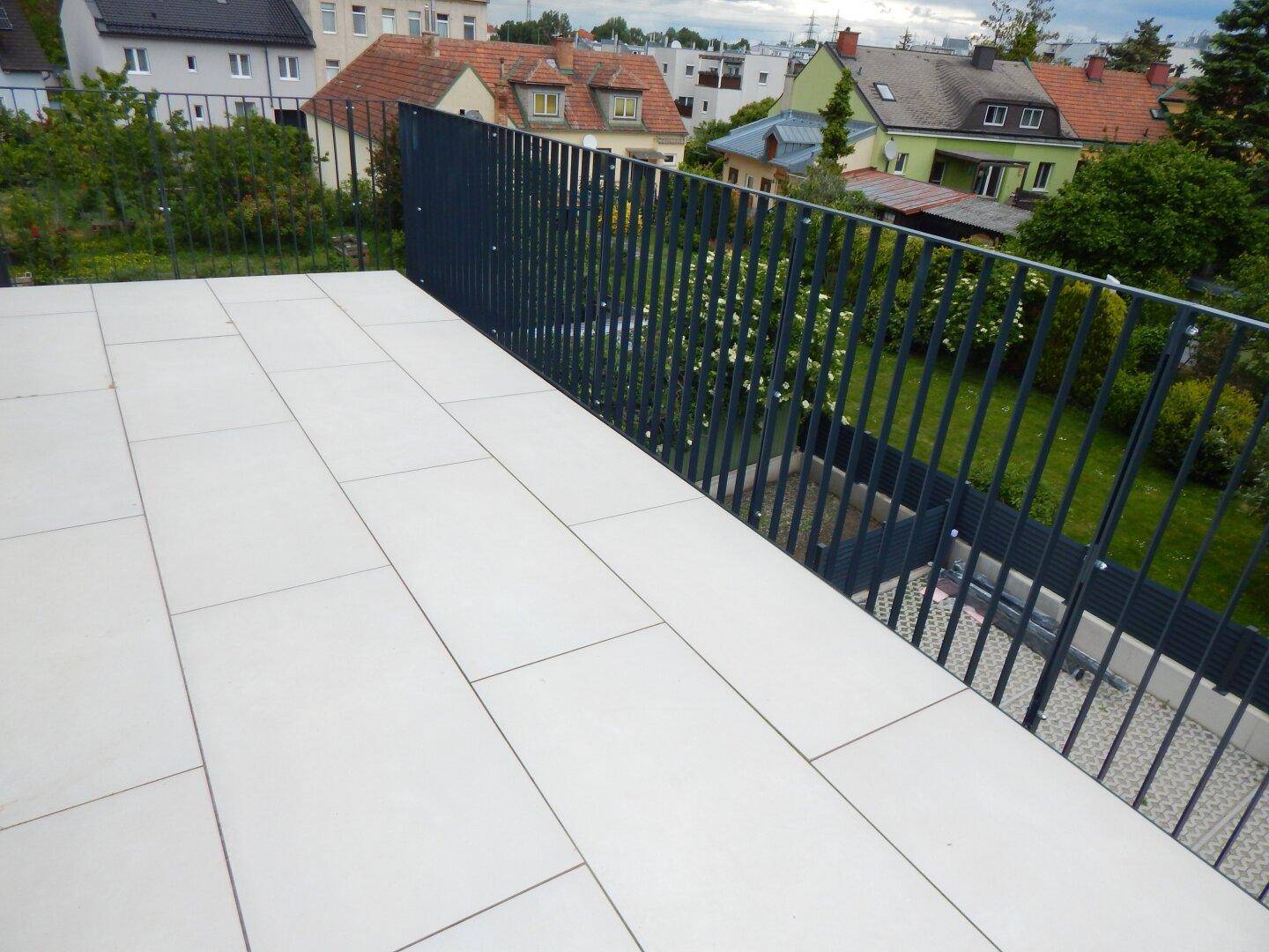 Großer Balkon mit hellen Fliesen und weitem Blick über die Nachbarschaft und Gärten.