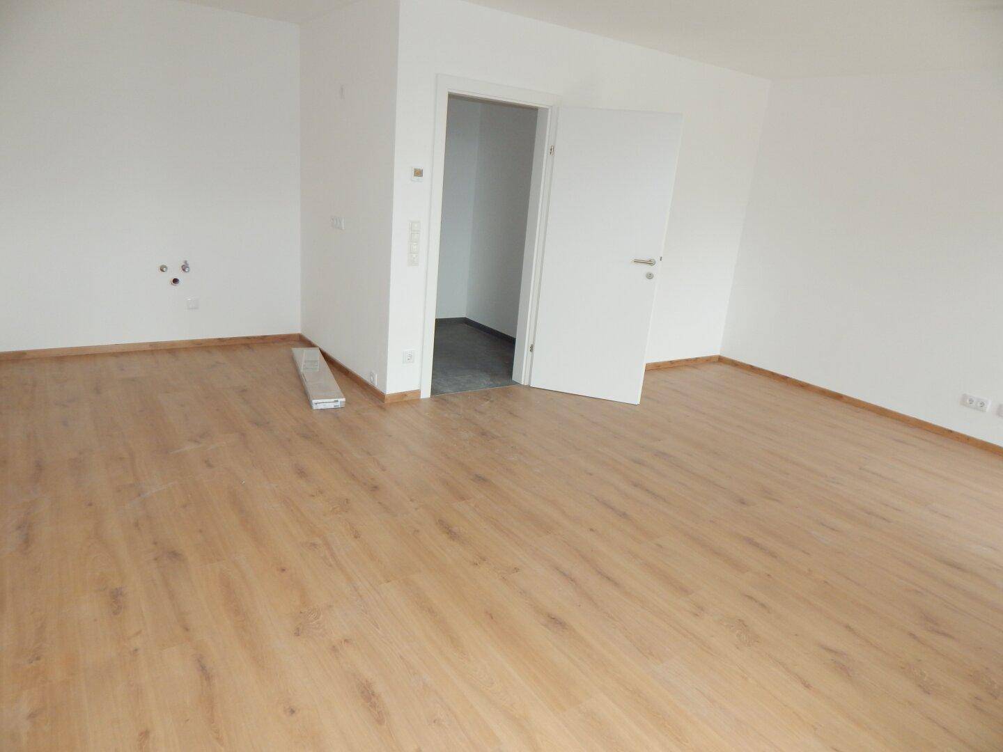 Leerer Raum mit Laminatboden und weiß gestrichenen Wänden, bereit zum Einzug.