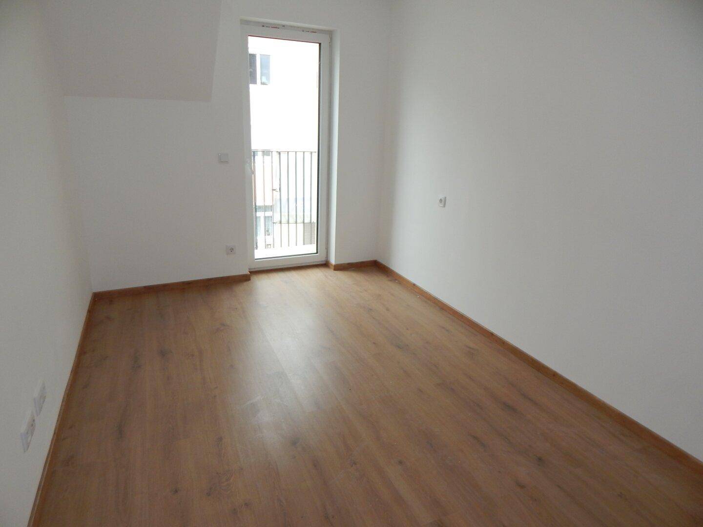 Helles Schlafzimmer mit Laminatboden und direktem Zugang zu einem kleinen Balkon.