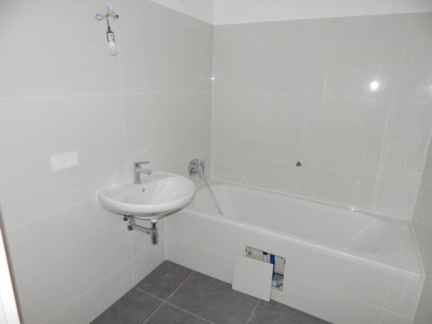 Modernes Badezimmer mit Badewanne, Waschbecken und hellgrauen Fliesen an Wänden und Boden.