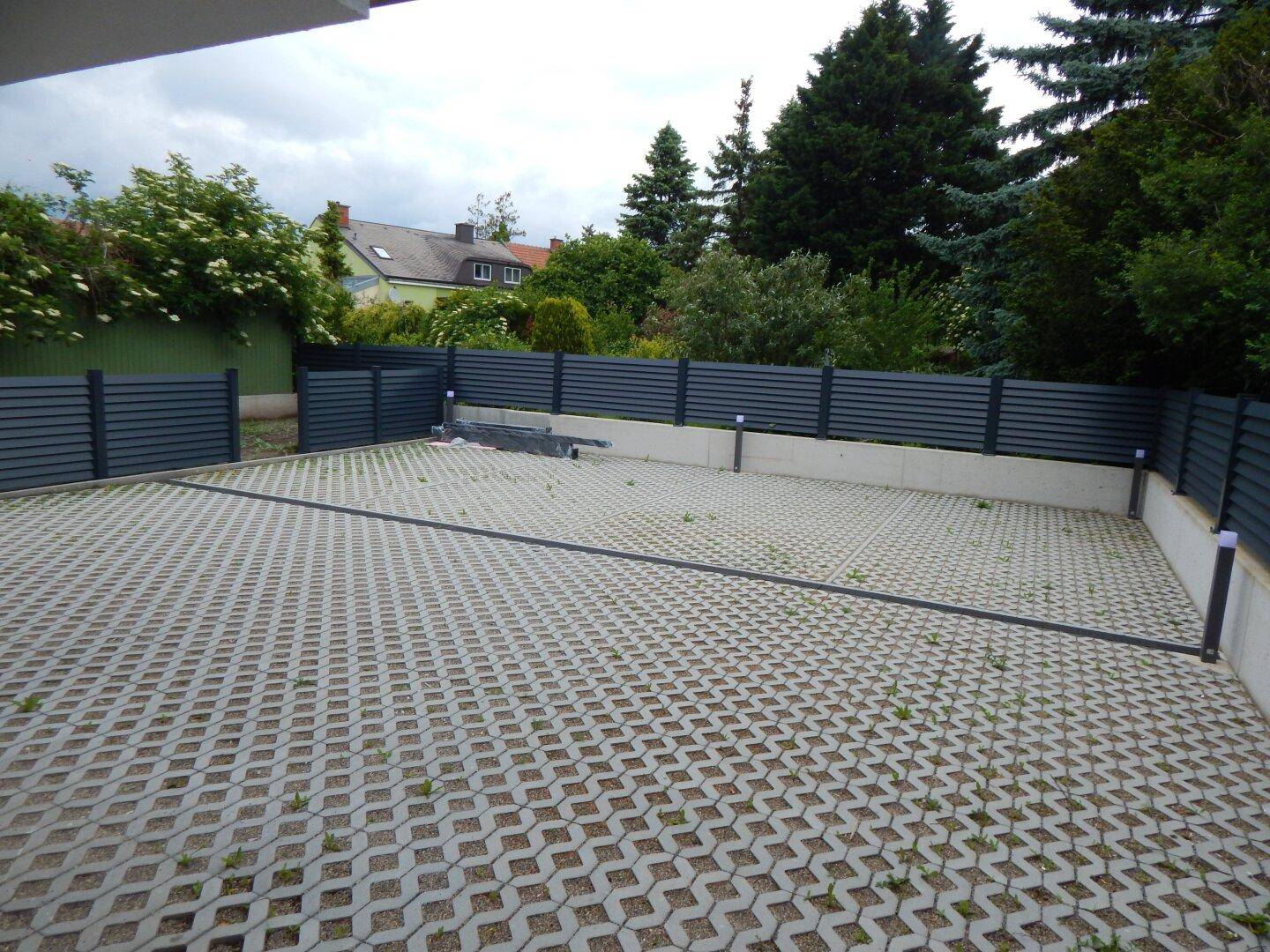 Großer Außenparkplatz mit Rasengittersteinen und einer modernen dunklen Zaunanlage.