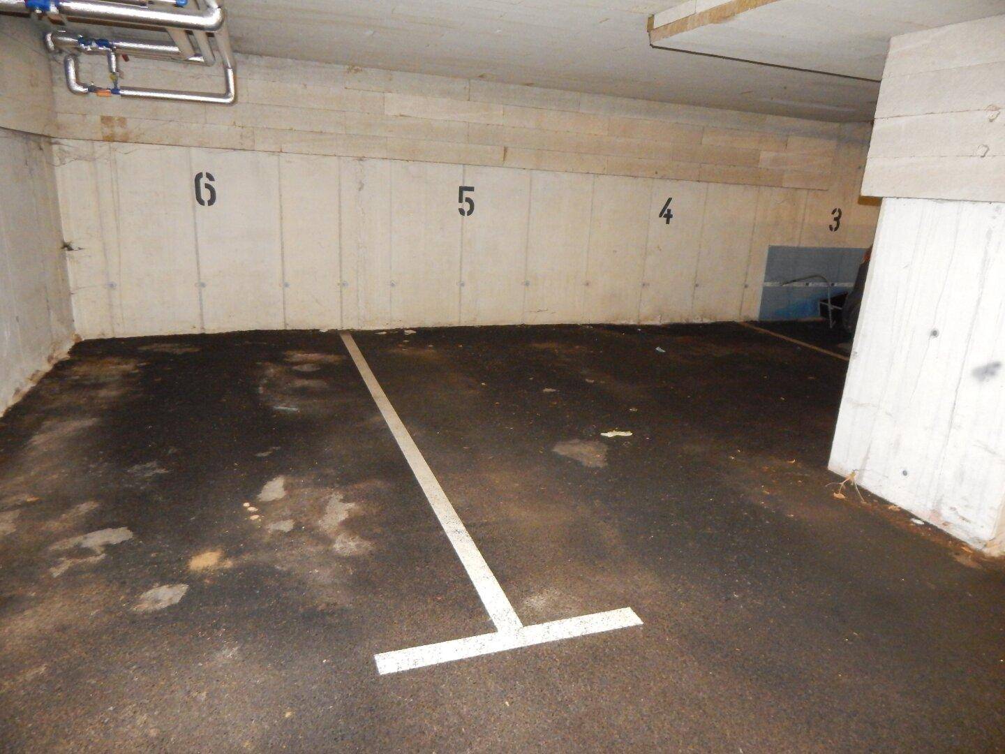 Leerer Stellplatz in der Tiefgarage mit nummerierten Wänden und Betonpfeilern.
