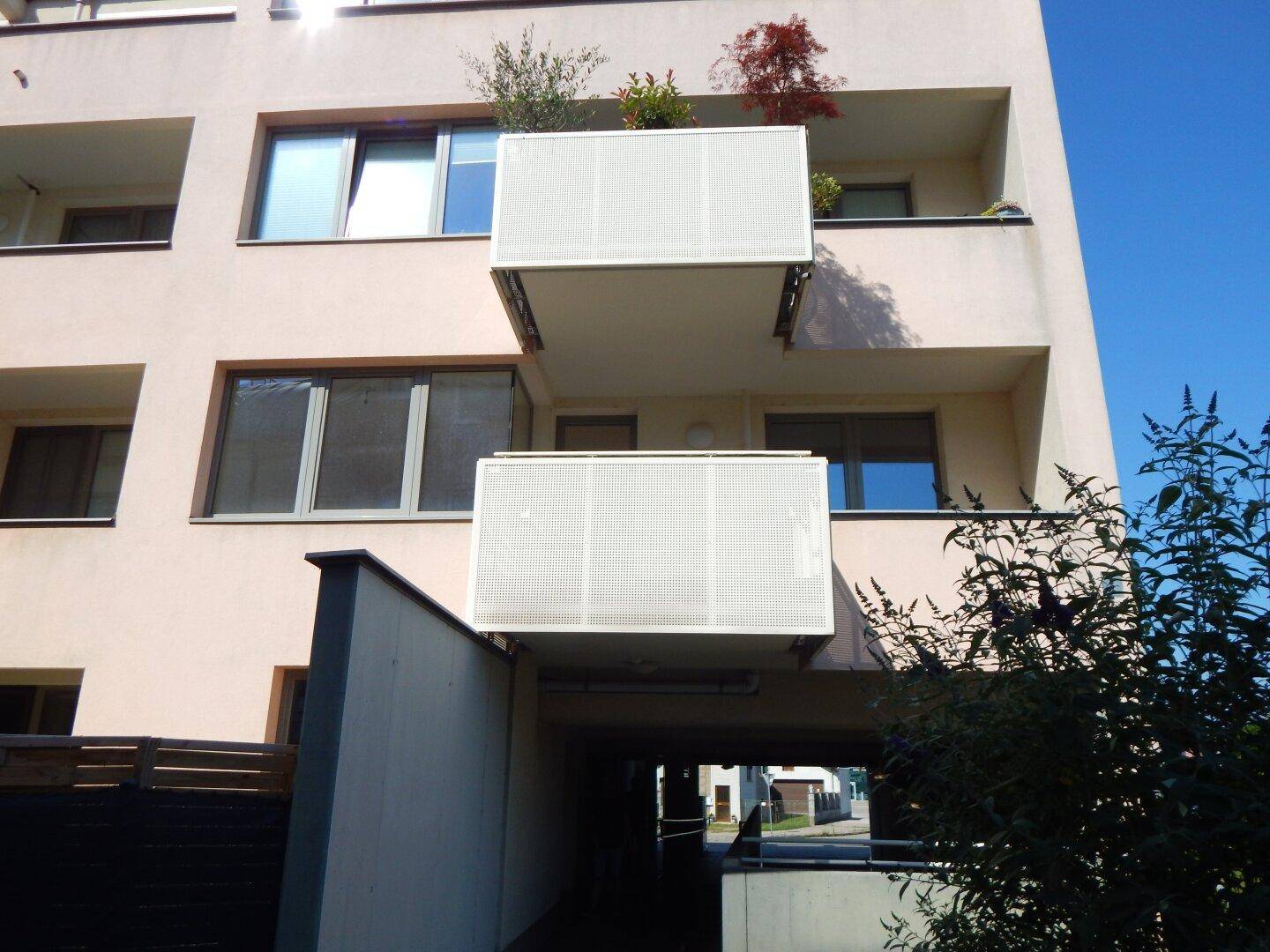 Detailansicht der modernen Fassade mit Balkonen und der Einfahrt zur Tiefgarage.
