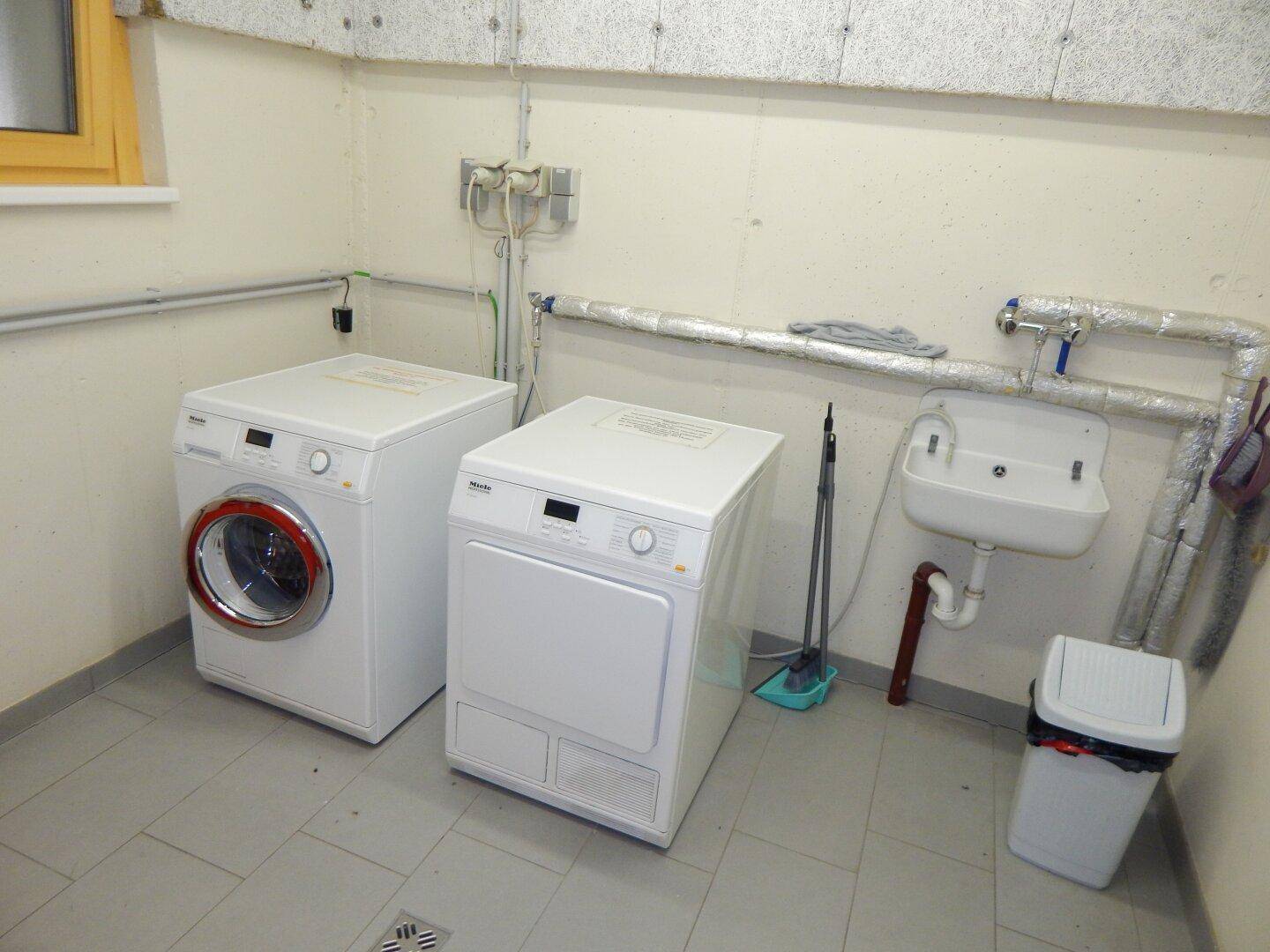 Gemeinschaftlicher Waschraum mit Waschmaschine, Trockner und Waschbecken.