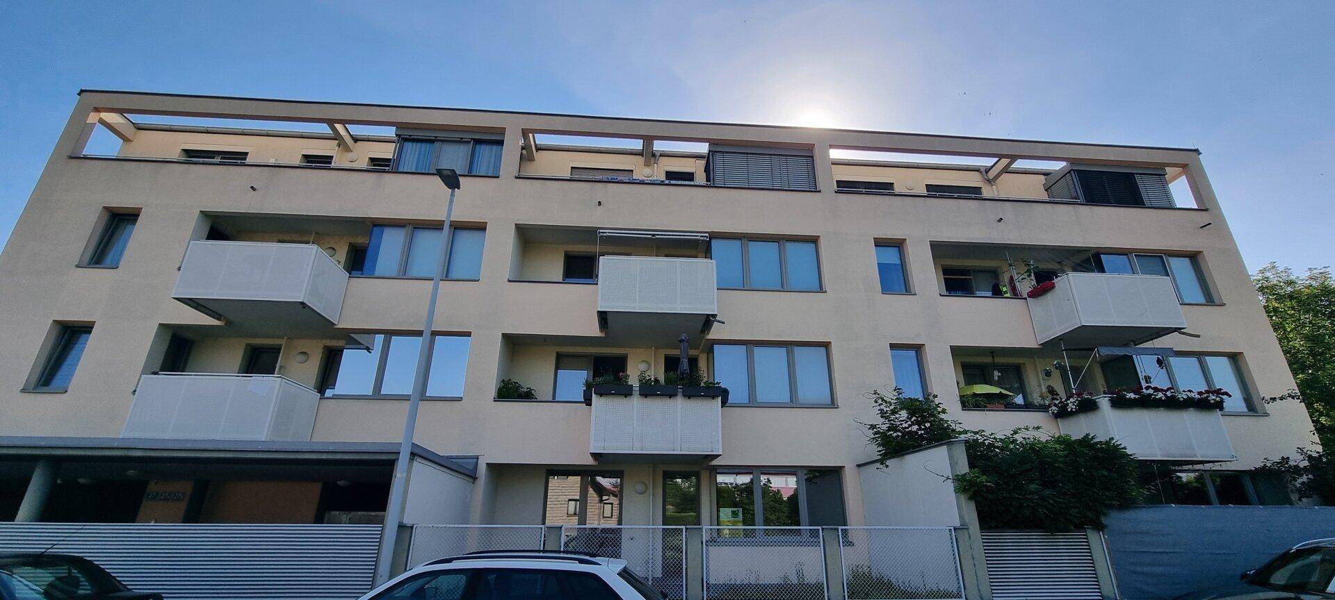 Fassade eines modernen Wohngebäudes mit Balkonen und großen Fenstern bei Sonnenschein.