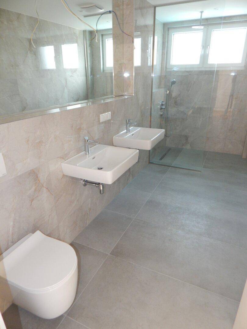Helles Badezimmer mit Doppelwaschbecken, ebenerdiger Dusche und modernen Fliesen.