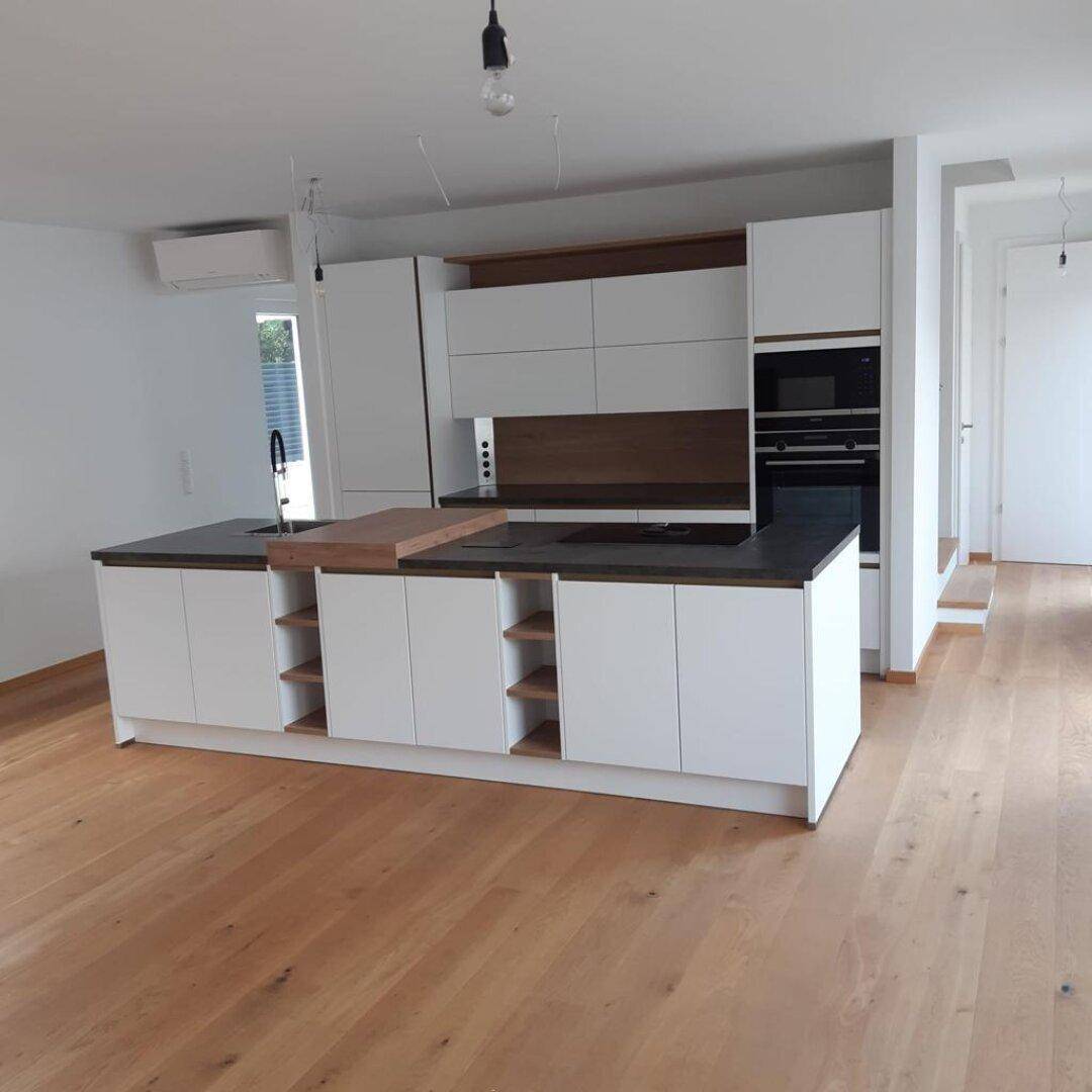 Geräumige, moderne Küche mit Kücheninsel, weißen Schränken und hellem Holzfußboden.
