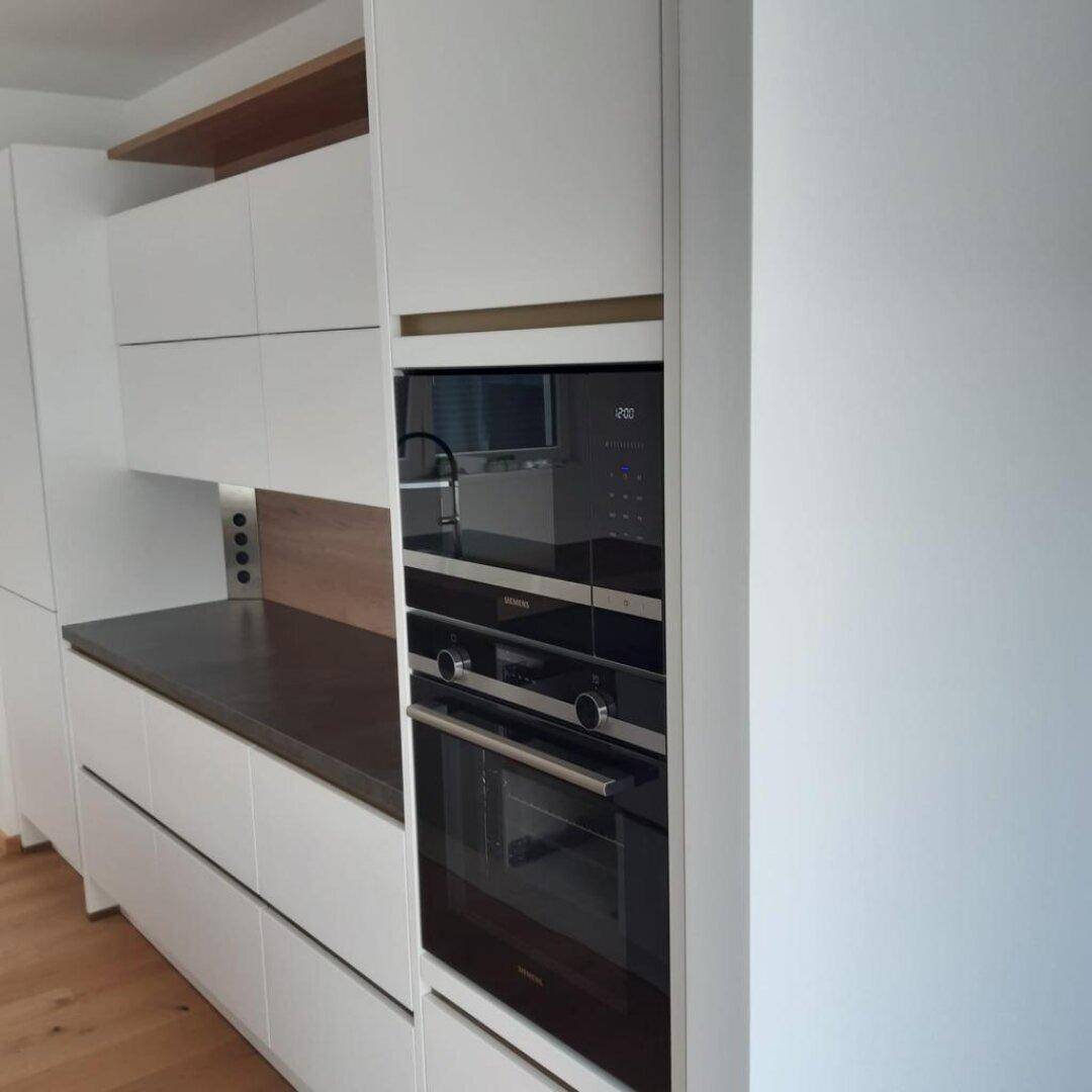Integrierte Siemens-Backöfen in einer modernen Küche mit weißen Schränken und Holzdetails.