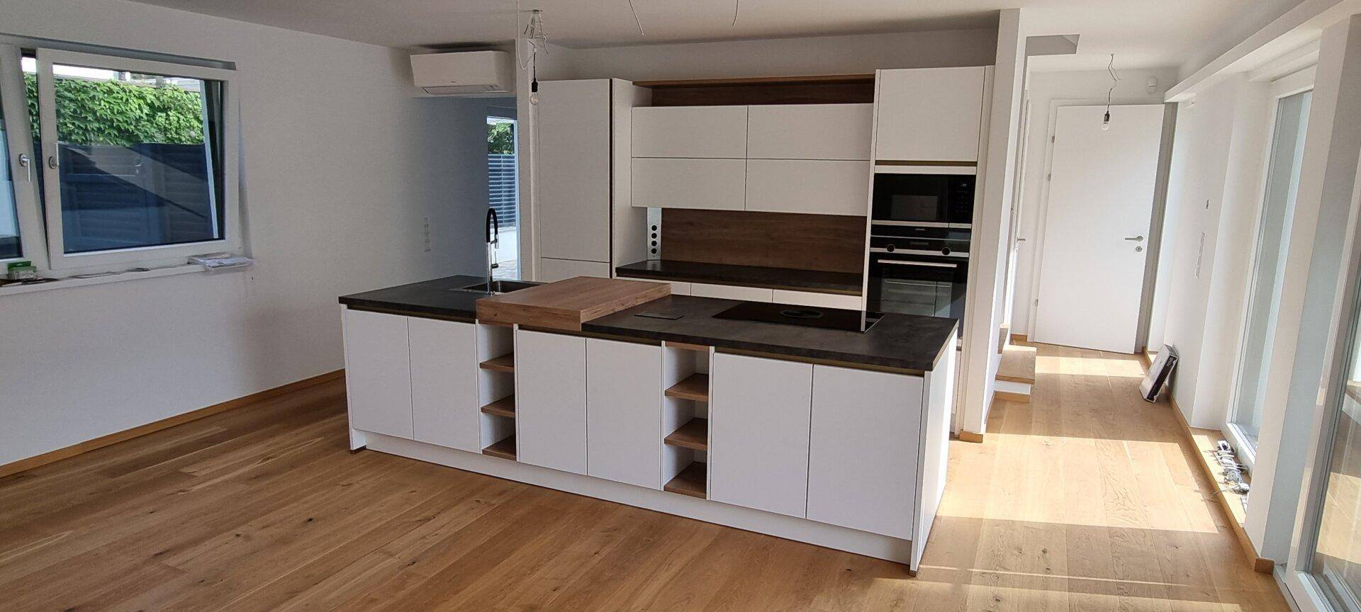 Helle, offene Küche mit modernen Geräten, Holzboden und viel Tageslicht.