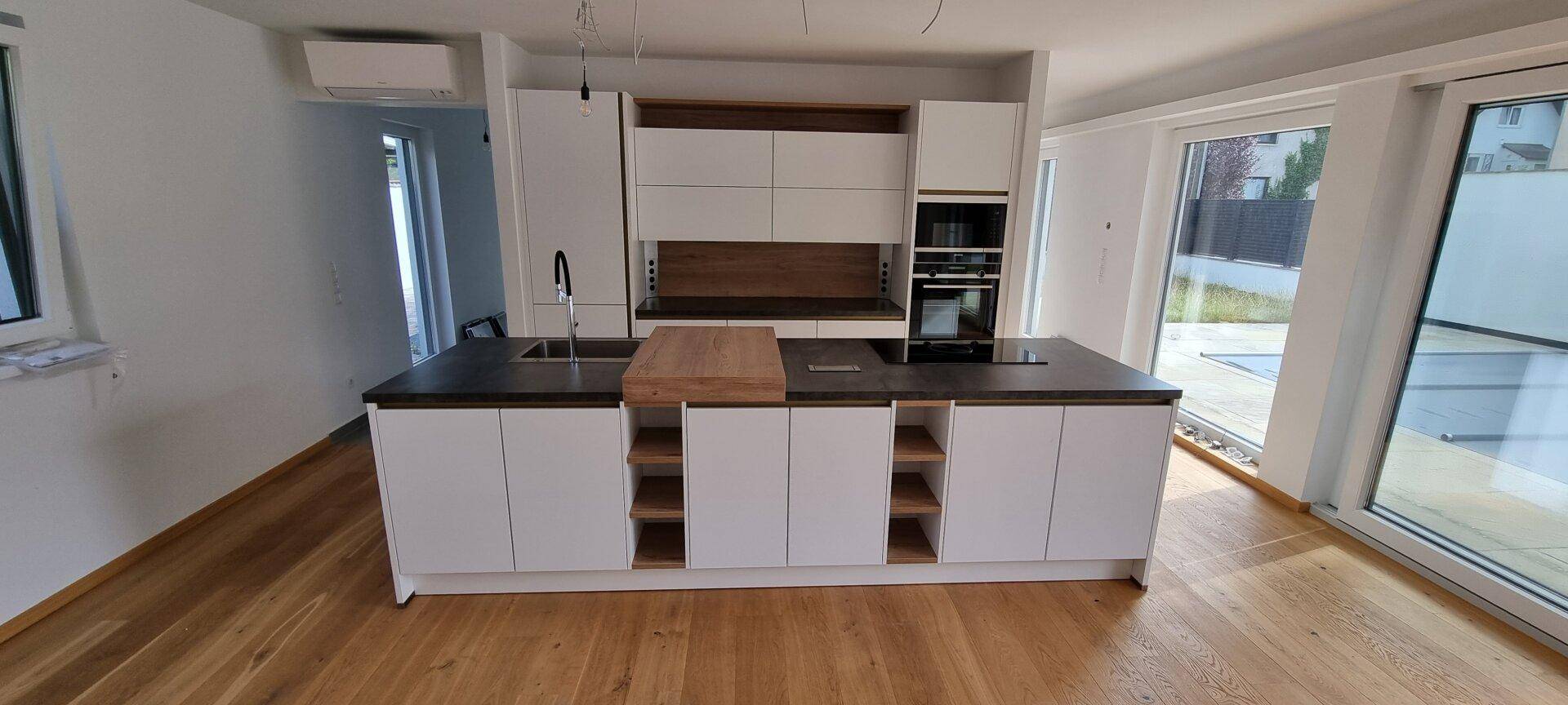 Moderne Einbauküche mit weiß-holz Design, Kücheninsel und Zugang zur Terrasse.