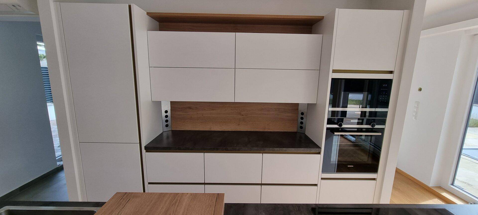 Moderne Einbauküche mit weißen Fronten, dunkler Arbeitsplatte und integrierten Elektrogeräten.