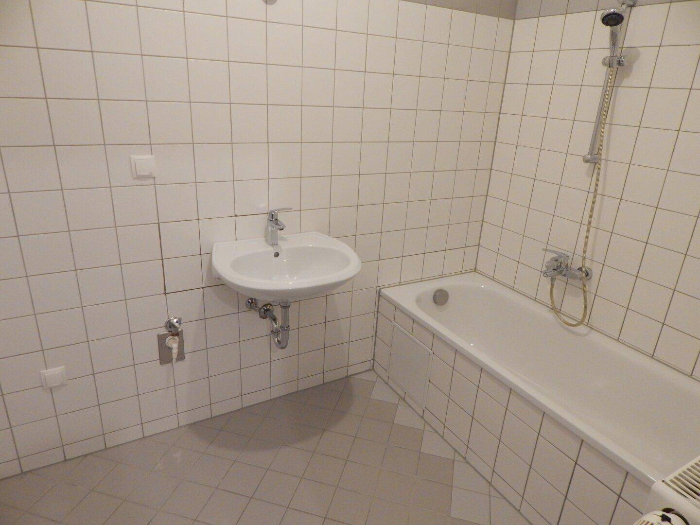 Gefliestes Badezimmer mit Badewanne, Waschbecken und Duschvorrichtung.
