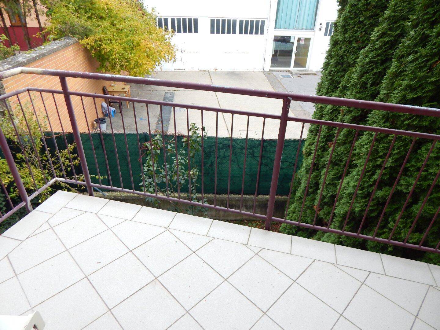 Balkon mit Fliesenboden und Blick auf einen Hinterhofbereich mit Mauer.