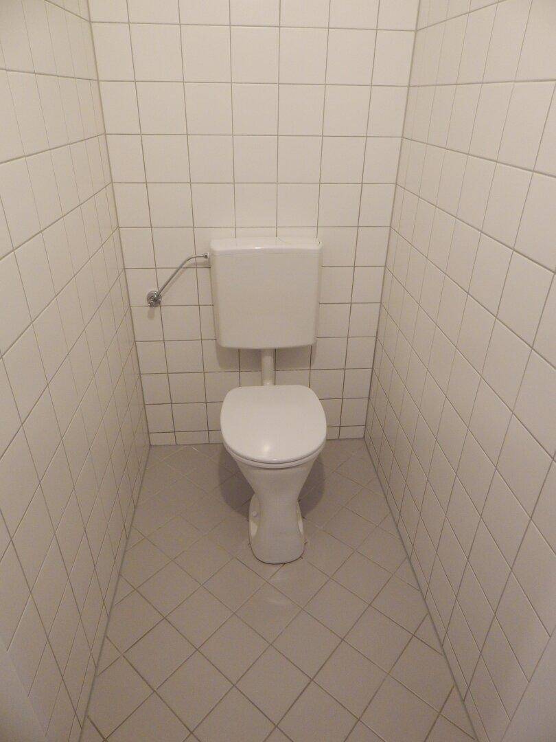 Separate Toilette mit weißen Fliesen an Wänden und Boden.