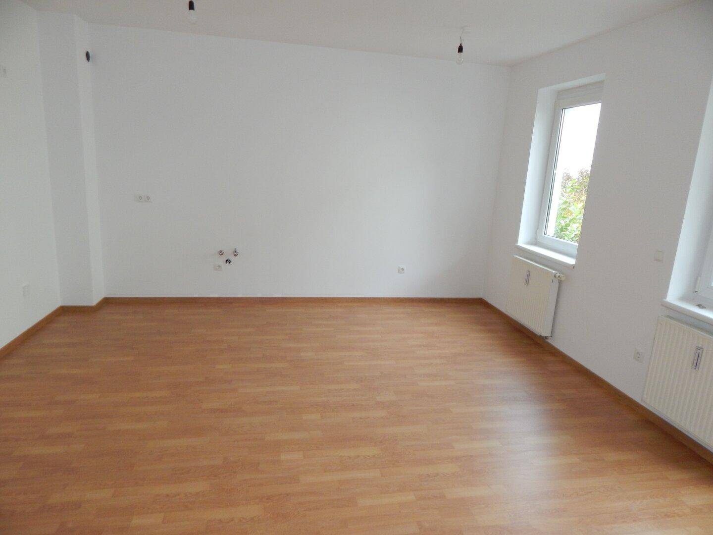 Helles, leeres Zimmer mit Laminatboden und zwei Fenstern, bereit zur Einrichtung.