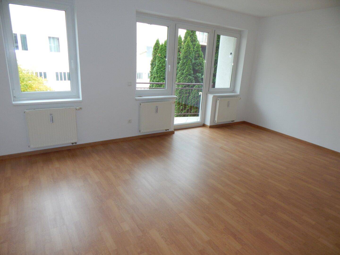 Geräumiges, helles Zimmer mit Laminatboden und Fenstern mit Blick ins Grüne.