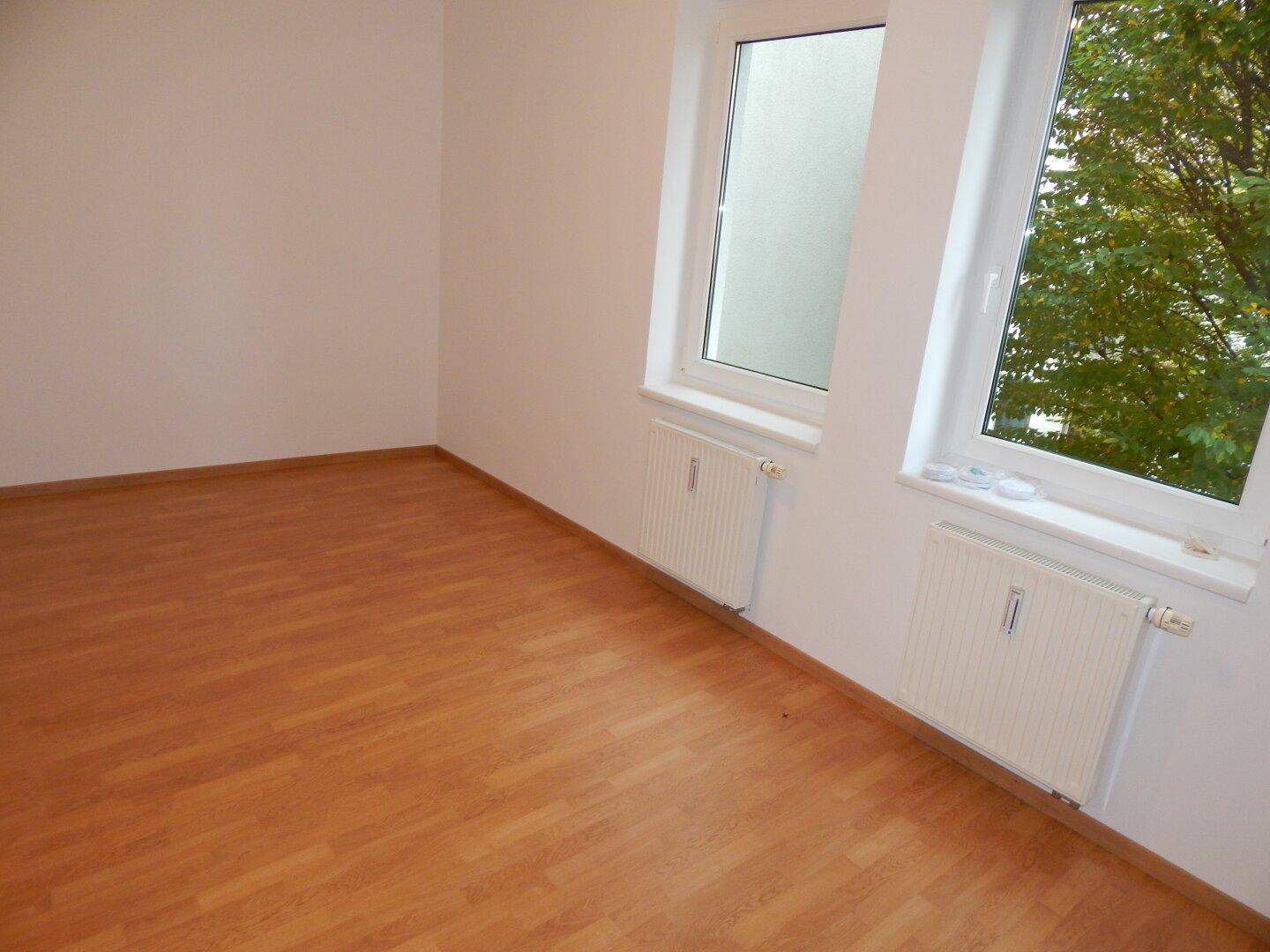Helles Zimmer mit Laminatboden und zwei Fenstern, ideal als Schlaf- oder Arbeitszimmer.