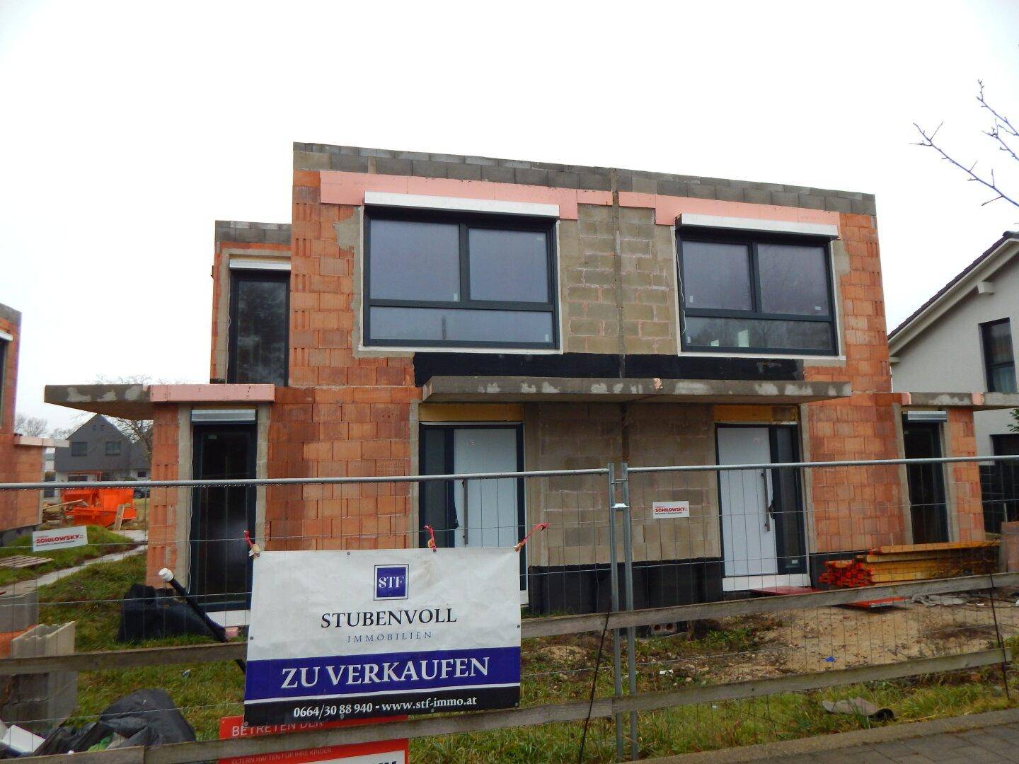 Außenansicht eines Neubaus im Rohbauzustand mit installierten Fenstern und einem Verkaufsbanner.