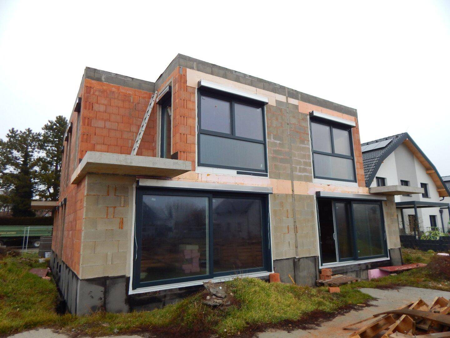 Seitenansicht des Neubaus mit großen Schiebetüren im Erdgeschoss und sichtbaren Bauelementen.