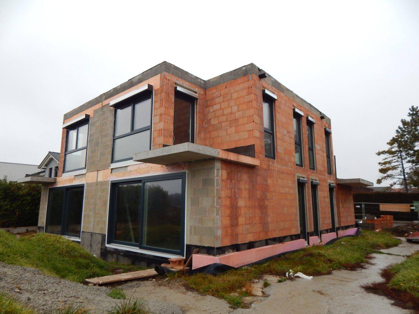 Rückansicht des im Bau befindlichen Hauses mit unverputzten Ziegelwänden und mehreren Fensteröffnungen.
