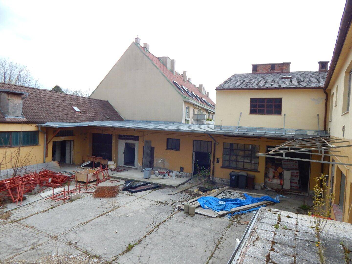 Innenhof eines Gebäudekomplexes mit verschiedenen Eingängen und Baumaterialien.