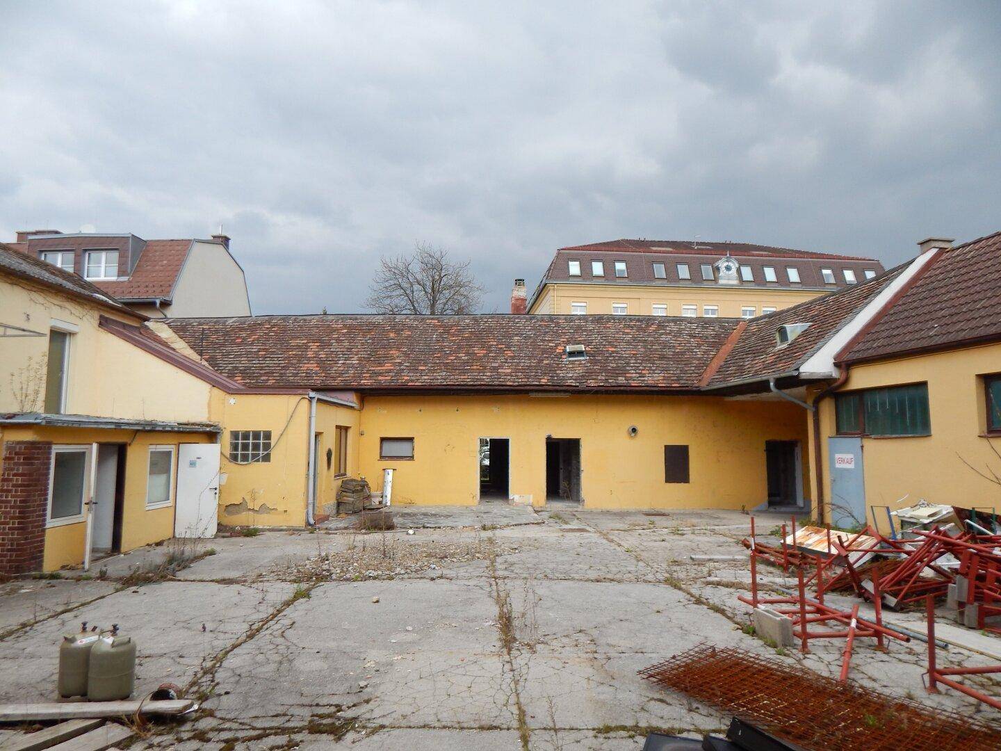 Blick auf den Innenhof eines älteren Gebäudes mit mehreren Zugängen und einem bewölkten Himmel.