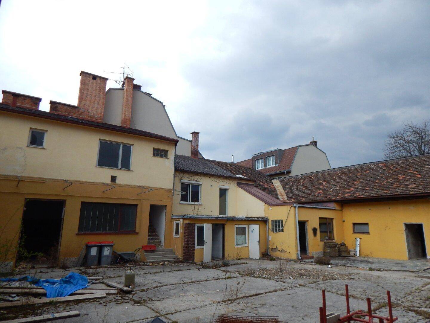 Verschiedene Gebäudeteile um einen Innenhof mit sichtbaren Schornsteinen und Fenstern.