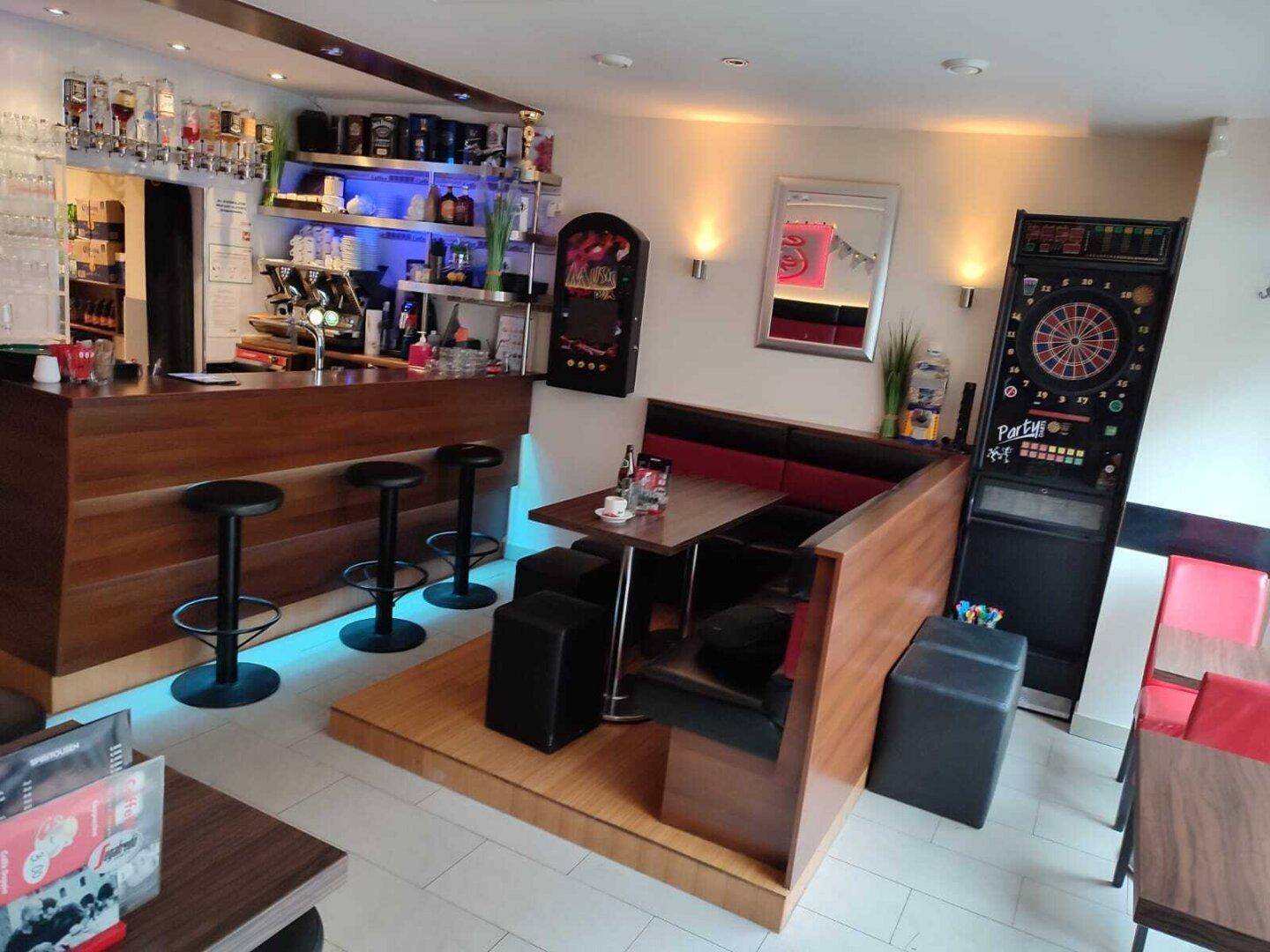Gemütliche Bar mit Holztresen, Hockern und Sitznischen, beleuchtet mit blauen LEDs.