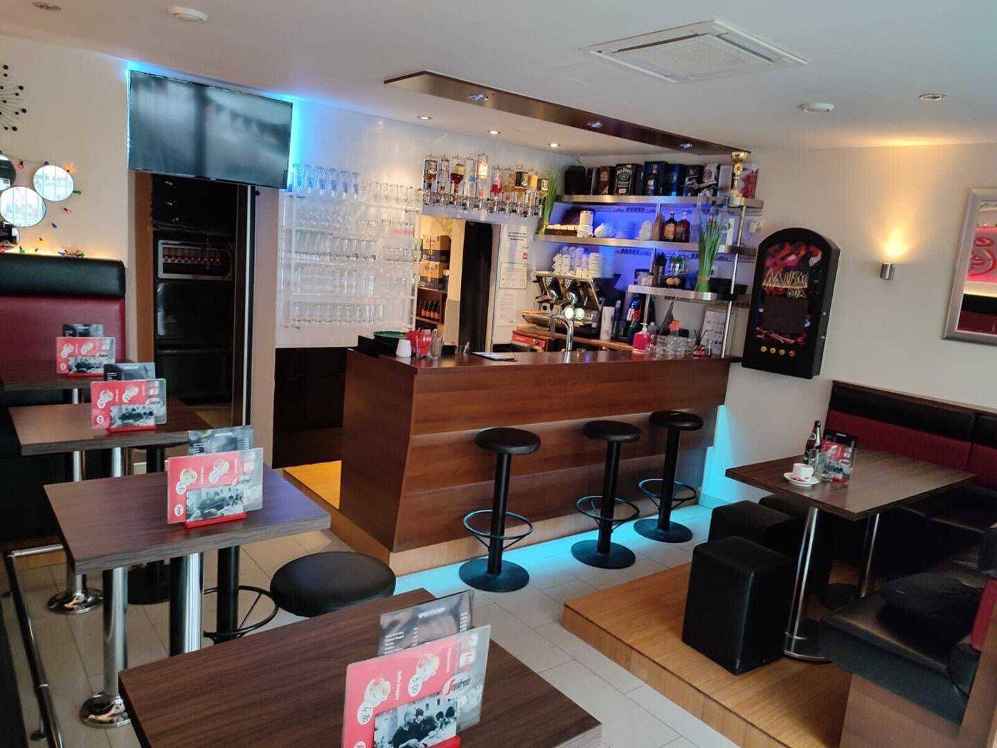 Innenansicht der Bar mit Holztresen, Glasregalen und verschiedenen Sitzgelegenheiten.