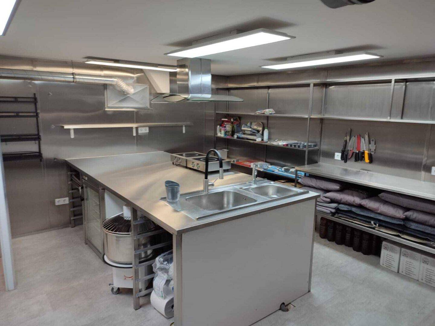Weitläufige Industrieküche mit Edelstahlregalen, Arbeitsflächen und professionellen Geräten.