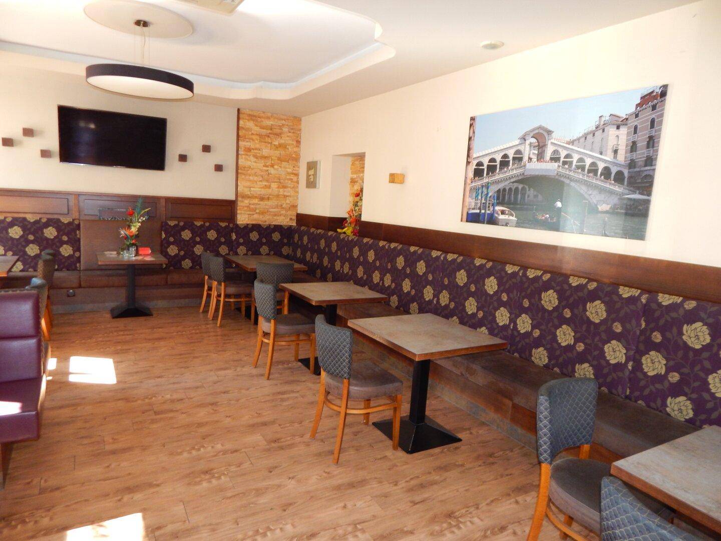 Gemütlicher Restaurantbereich mit gepolsterten Sitzbänken, Holzboden und einem großen Wandbild als Dekoration.