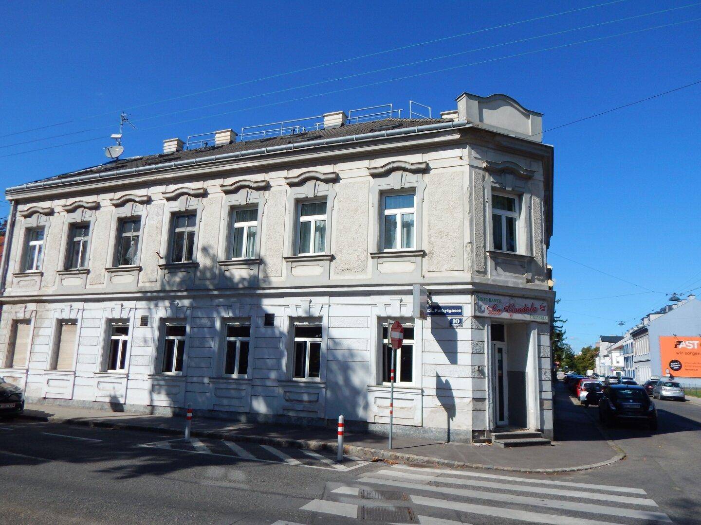 Historisches Eckgebäude mit klassischer Fassade und großen Fenstern an einer belebten Kreuzung.